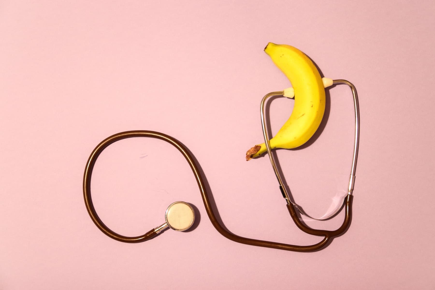 A stethoscope laid out around a banana on a pink background